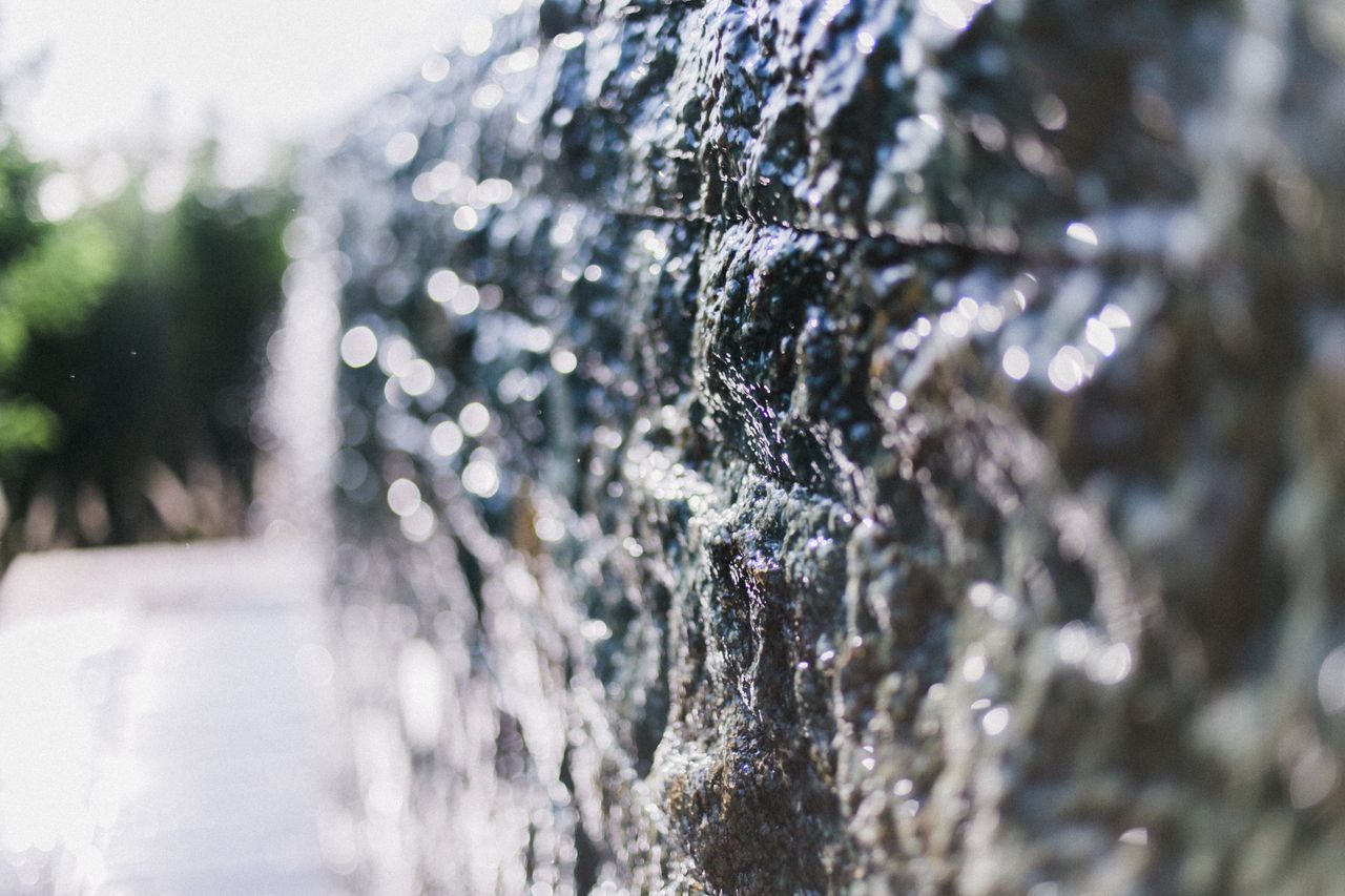 Closeup of rough stone wall with cracks in drops of water glistening in bright sunlight